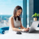 CGI-rendered Dell laptop and black wireless mouse integrated into a stock photo of a woman working at a modern office table with a city skyline in the background, created by Digital Imaging Group